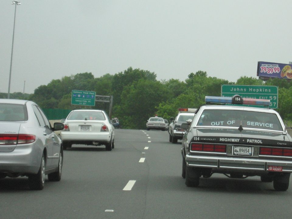 Black Highway Patrol Caprice and silver cars on highway near Johns Hopkins sign
