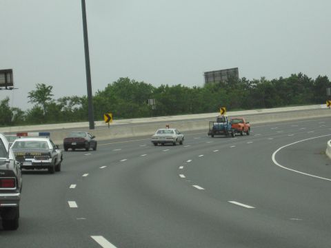 1991 Ford Crown Victoria - A highway patrol car leads a procession of vehicles on a multi-lane road.
