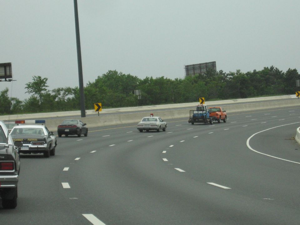 Police car following white car and pickups on curving multi-lane highway