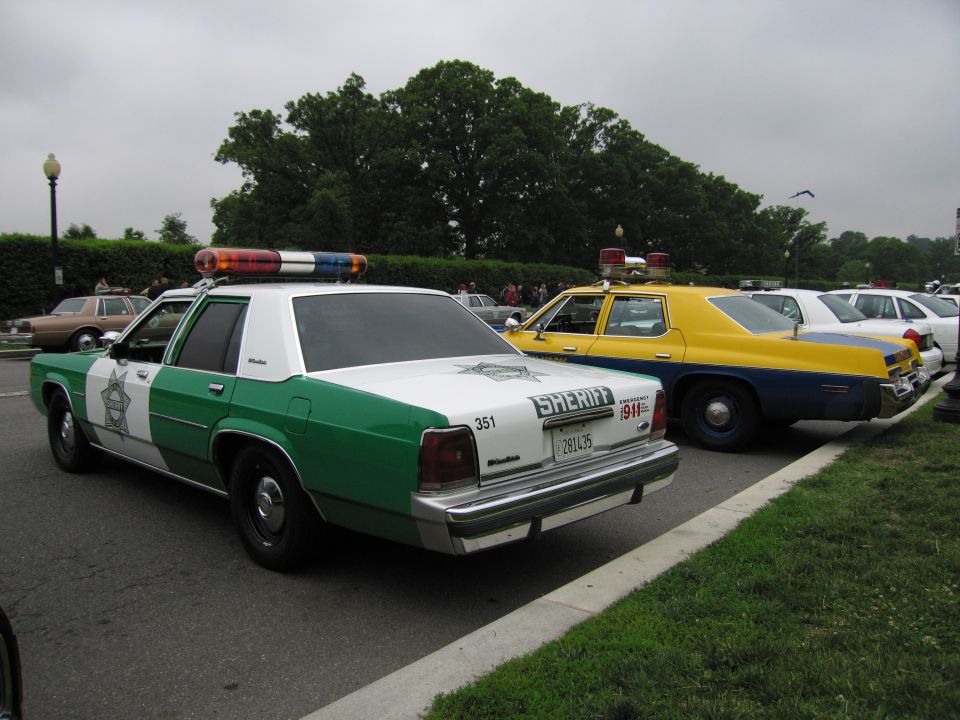 Green and white Ford LTD Crown Victoria Sheriff sedan, rear three-quarter view, beside a yellow sedan
