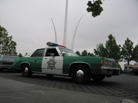 1991 Ford Crown Victoria - A vintage police car is parked outdoors with a distinctive monument in the background.