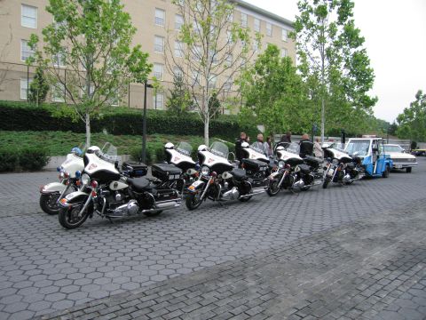 1991 Ford Crown Victoria - A line of police motorcycles is parked on a paved area, with a tow truck and car in the background.