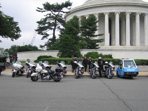 1991 Ford Crown Victoria - A line of police motorcycles and a small blue police vehicle are parked in front of a grand building.