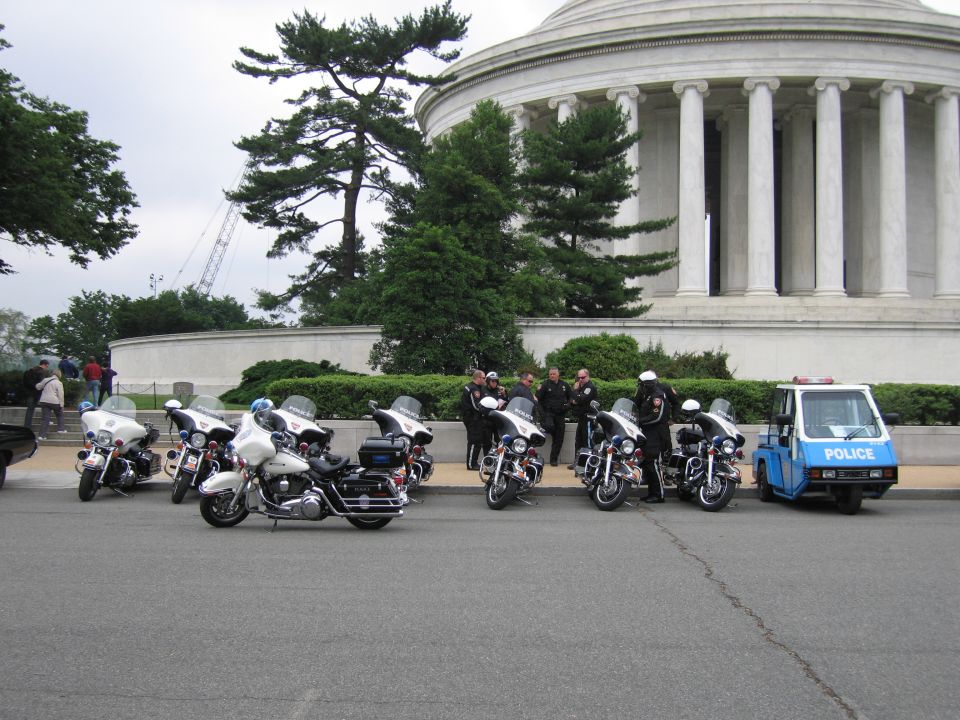 Police motorcycles and a blue police cart parked in front of a domed memorial