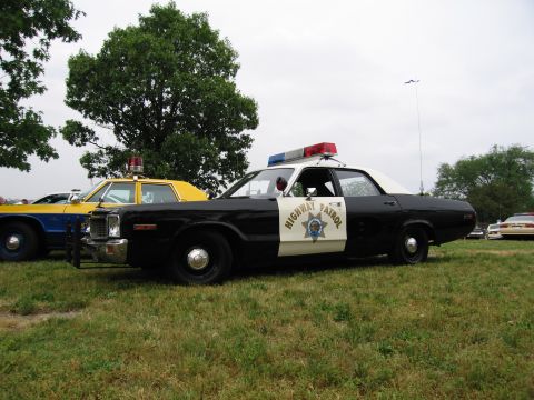 1991 Ford Crown Victoria - A black and white police car with a light bar is parked on a grassy field next to a yellow car.