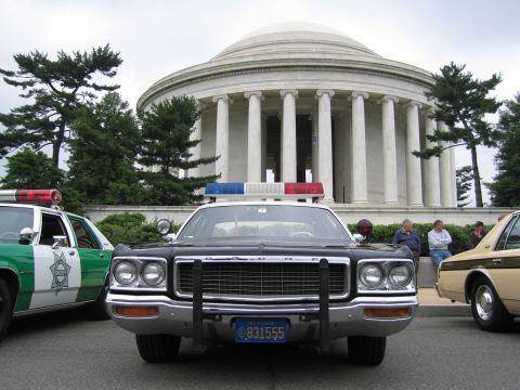 1991 Ford Crown Victoria - A black police car is parked in front of a domed building, with another police car and a tan car visible.