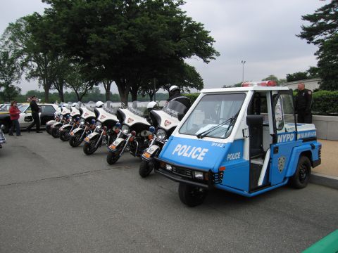 1991 Ford Crown Victoria - A line of police motorcycles and a three-wheeled NYPD vehicle are parked outdoors.