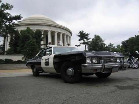 1991 Ford Crown Victoria - This vintage police car is parked in front of a large domed building, with a motorcycle nearby.