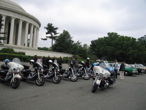 1991 Ford Crown Victoria - A line of police motorcycles and several police cars are parked outdoors.