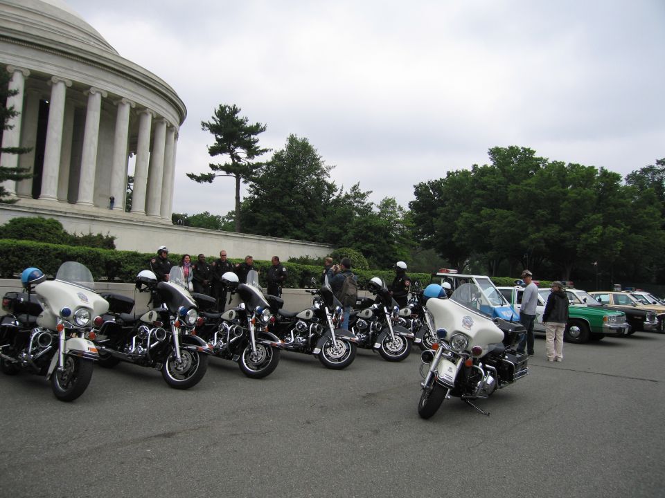 Row of police motorcycles parked before domed memorial with people and cars behind