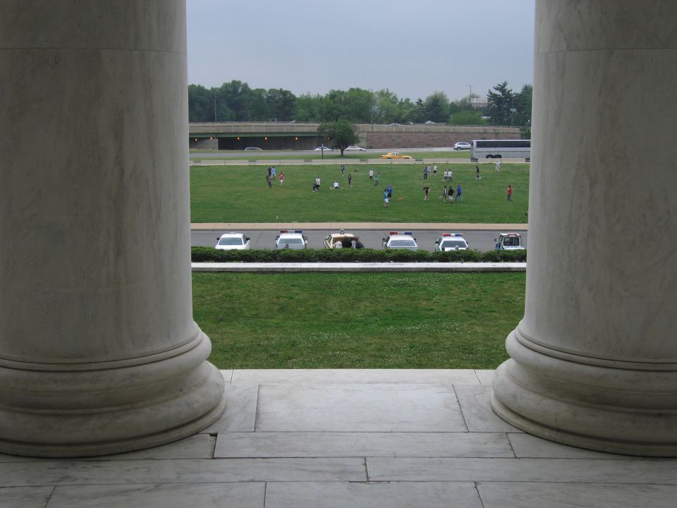View between two marble columns of police cars and people on a green mall lawn