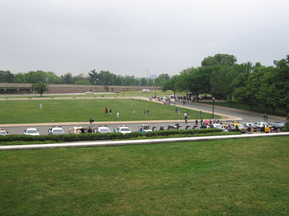 Elevated view of police cars and motorcycles parked along a curving drive on green lawn