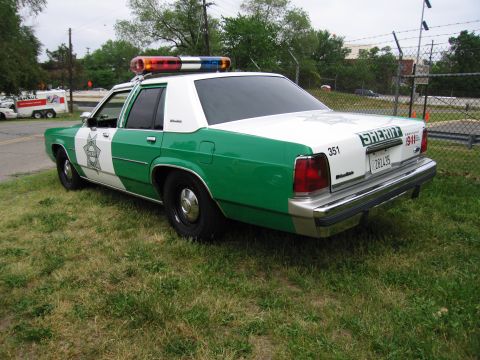 1991 Ford Crown Victoria - This sheriff's car, marked with 'SHERIFF' and '911', has a distinctive green and white paint scheme and emergency lights on the roof.