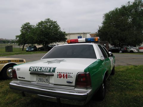 1991 Ford Crown Victoria - Rear view of a 1991 Ford Crown Victoria police car with 'SHERIFF' markings and emergency lights.