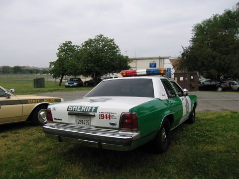 1991 Ford Crown Victoria - A Sheriff's car with a light bar is parked next to a State Police vehicle on a cloudy day.
