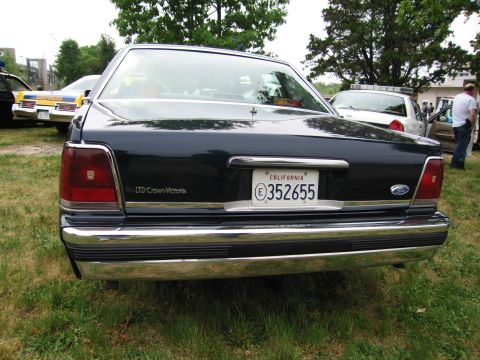 1991 Ford Crown Victoria - The rear of a dark-colored Ford LTD Crown Victoria is shown, parked on grass with other vehicles nearby.