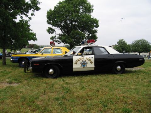 1991 Ford Crown Victoria - A vintage police car with "HIGHWAY PATROL" text and emblem on its side is parked on grass next to another vehicle.