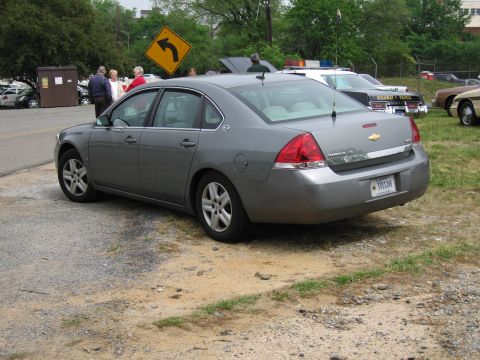 1991 Ford Crown Victoria - A gray Chevrolet Impala is parked on a gravel lot next to a police car.