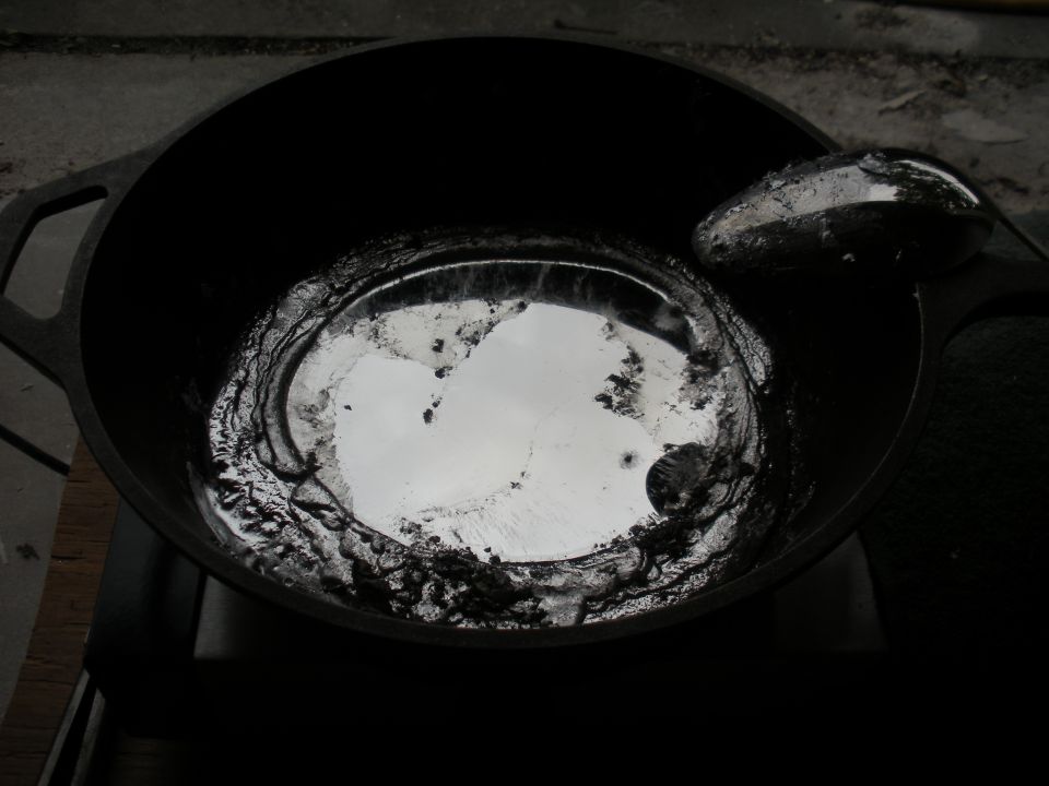 Molten metal pooling in a cast iron pot with a ladle nearby