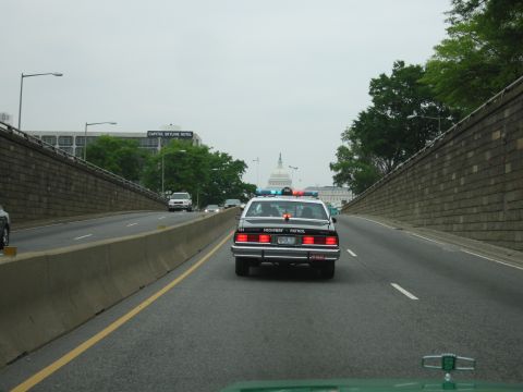 1991 Ford Crown Victoria - Highway Patrol car with lights on, driving on a highway with the Capitol building visible.
