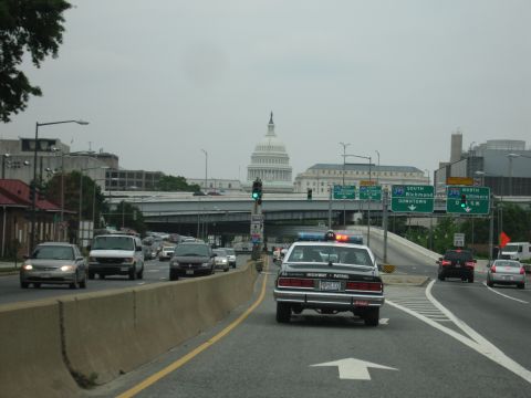 1991 Ford Crown Victoria - A highway patrol car drives on a busy road with the U.S. Capitol building visible in the distance.