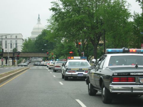 1991 Ford Crown Victoria - Police vehicles form a procession on a city street, with the Capitol building in the distance.