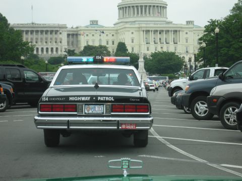 1991 Ford Crown Victoria - A Chevrolet Caprice police car is parked in a lot with other vehicles, with the Capitol building in the background.