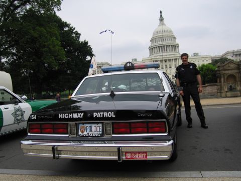 1991 Ford Crown Victoria - A police officer stands next to a highway patrol car with the US Capitol building in the background.