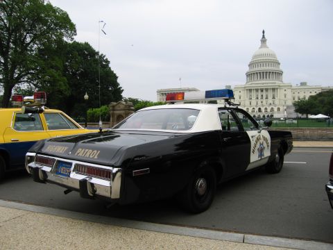 1991 Ford Crown Victoria - A vintage police car with 'HIGHWAY PATROL' markings is seen from the rear, with another vehicle and the Capitol building in the background.