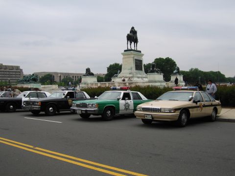 1991 Ford Crown Victoria - Several police vehicles are lined up in front of a monument, possibly for a parade or event.