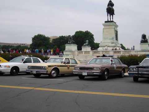1991 Ford Crown Victoria - Police cars are parked in front of a monument with a crowd of people in the background.