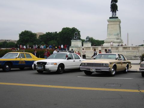 1991 Ford Crown Victoria - Several police vehicles are parked in front of a monument on an overcast day.