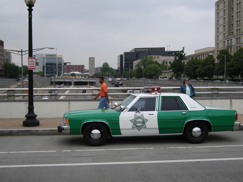 Green-and-white sheriff sedan with star shield parked on a city street