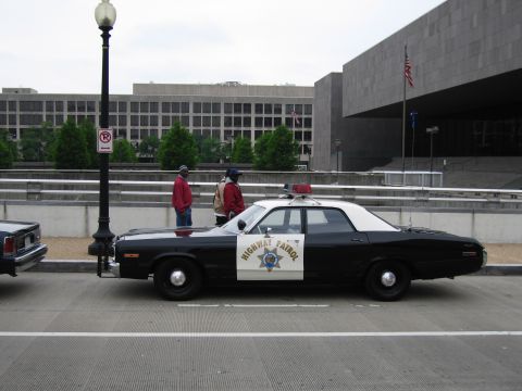 1991 Ford Crown Victoria - Side view of a black and white 1977 Dodge Monaco police car with "HIGHWAY PATROL" text on the door.