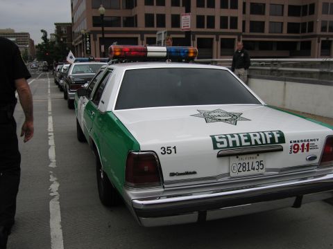 1991 Ford Crown Victoria - A line of sheriff's vehicles, including a 1991 Ford Crown Victoria, are parked on a street.