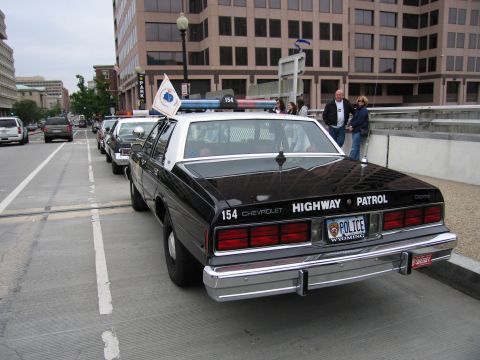 1991 Ford Crown Victoria - A line of police cars are parked on a city street, with buildings in the background.
