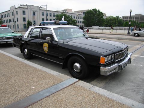1991 Ford Crown Victoria - A black and white 1991 Ford Crown Victoria police car is parked on the street, with another police car visible to its left.