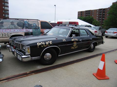 1991 Ford Crown Victoria - This black police car has "POLICE" written on its side. Other vehicles are visible in the background.