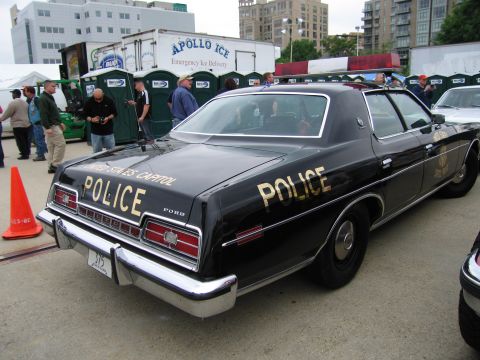 1991 Ford Crown Victoria - A vintage police car is parked outdoors with portable toilets and an ice truck in the background.