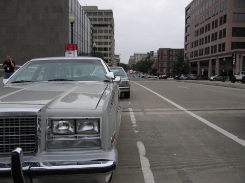 1991 Ford Crown Victoria - A silver police car with a red light bar is parked on a city street, with other vehicles visible in the background.