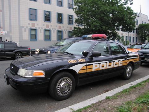 1991 Ford Crown Victoria - A police car with a light bar on top is parked on the street next to other vehicles.