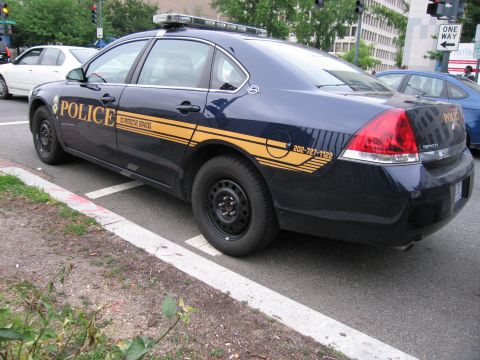 1991 Ford Crown Victoria - A dark blue police car with yellow accents and 'POLICE' markings is parked on the street.