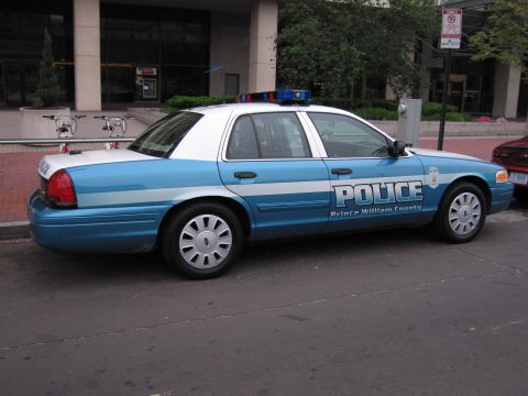 1991 Ford Crown Victoria - A blue and white police car is parked on the side of a street in front of a building.