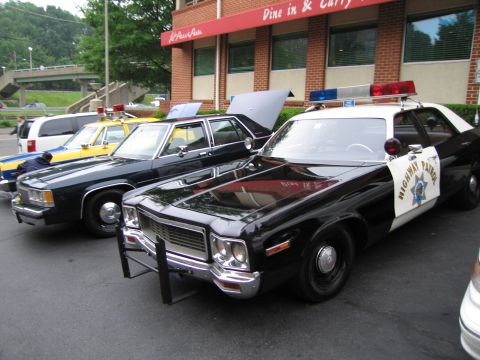 1991 Ford Crown Victoria - Several vintage police cars are lined up in front of a building with a red awning.