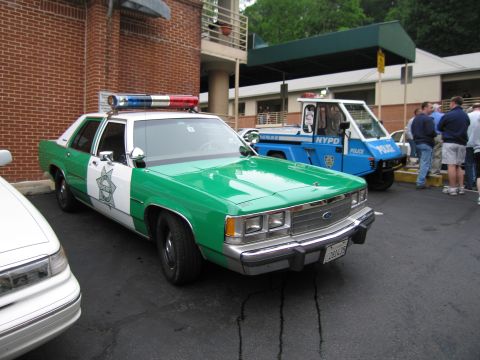 1991 Ford Crown Victoria - A green and white police car is parked next to a blue NYPD vehicle.