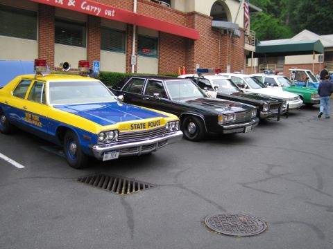 1991 Ford Crown Victoria - A line of police cars, including a vintage New York State Police vehicle, are parked in front of a brick building.