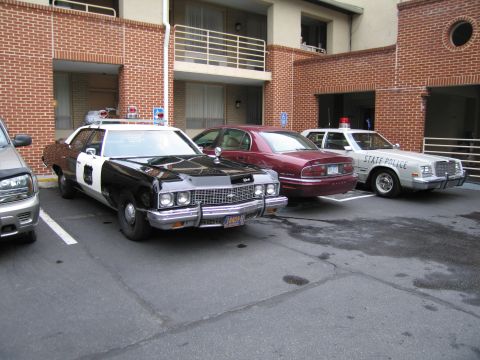 1991 Ford Crown Victoria - Three police cars are parked in a lot outside a brick building.
