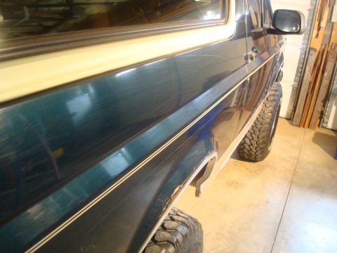 1995 Ford Bronco - Side view of a 1995 Ford Bronco, showing its dark green paint, beige trim, and chrome accent strip.