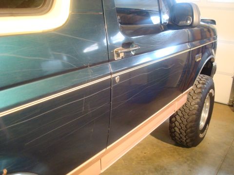 1995 Ford Bronco - The side of a dark green 1995 Ford Bronco shows extensive scratching across the paintwork.