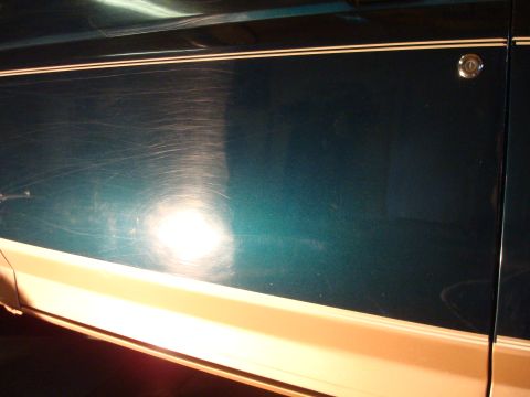 1995 Ford Bronco - Side panel of a teal vehicle a cream stripe and extensive surface scratches, with a door lock visible near the rear.